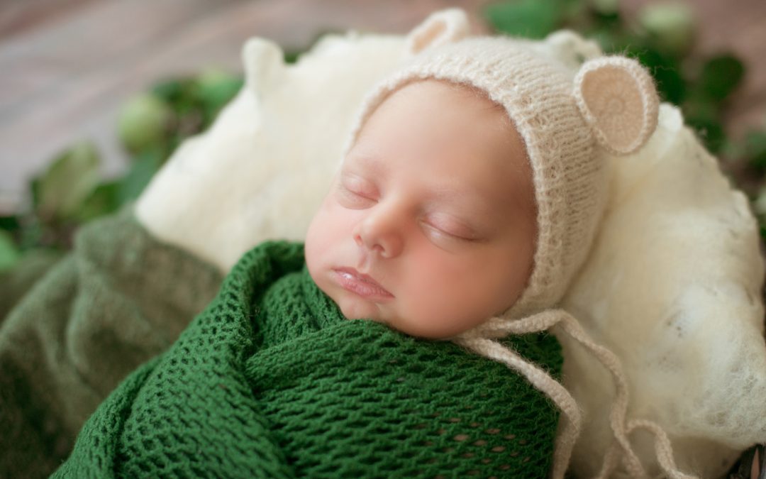 Choices to make for your newborn. Pic- a newborn baby wearing a cap and wrapped in a green blanket